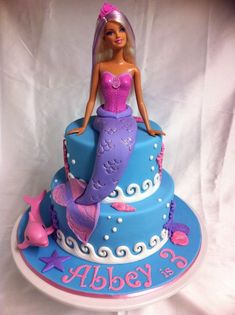 a barbie doll sitting on top of a blue and purple cake