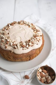 a white plate topped with a cake covered in frosting next to a bowl of nuts