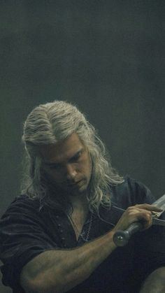 a man with long white hair holding a knife in his right hand and looking down