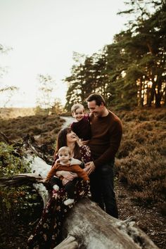 a family standing on a fallen tree trunk in the woods with their toddler girl