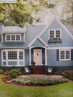 a blue house with white trim on the front door and two chairs in front of it