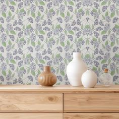 two vases sitting on top of a wooden dresser next to a wallpapered wall