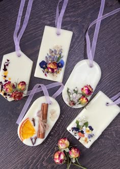 four ceramic tags decorated with dried flowers and herbs on a wooden table next to purple ribbon