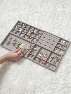 a woman is holding a tray full of jewelry on a white carpet with her hand