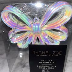 a colorful butterfly in a clear box on a marble counter top with a black tag hanging from it's side