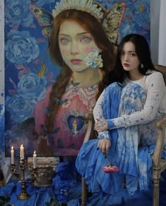 a woman sitting on a chair in front of a painting with candles and flowers around her