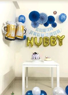 a table with balloons, cups and mugs on it in front of a happy birthday sign