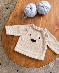 a knitted bear sweater sitting on top of a wooden table next to two balls of yarn