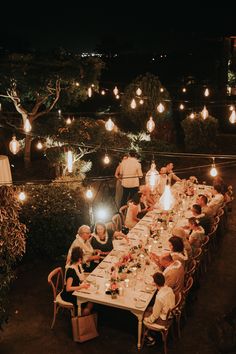 a group of people sitting around a dinner table with lit candles on the ceiling and hanging lights above them