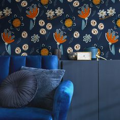 a blue couch sitting in front of a wall with flowers on it and a clock