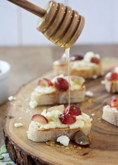 someone is drizzling cheese and fruit on top of crackers to make appetizers