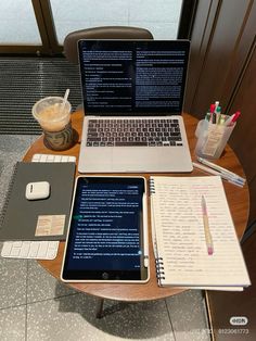 a laptop computer sitting on top of a wooden table next to a notebook and pen