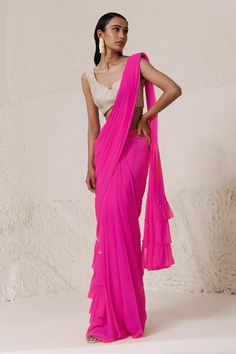 Neon pink pre-draped saree wit ruffle detailed hem and pallu with placement rhinestone embellishments. Paired with a padded silver rhinestone embellished blouse.
Components: 2
Pattern: Blouse: Embellished
Type Of Work: Rhinestone
Neckline: U Neck
Sleeve Type: Sleeveless
Fabric: Silk Georgette: Saree, Tissue: Blouse 
Color: Pink
Other Details: 
Padded and scallop trim blouse
Attached inner lining
Length: (in inches)
Saree: 44
Blouse: 14
Pleat detail pallu
Occasion: Sangeet - Aza Fashions Pink Lehenga With Ruffles And Traditional Drape, Pink Ruffled Lehenga For Diwali, Festive Pink Ruffled Sharara, Pink Pre-draped Saree With Ruffles For Wedding, Pink Ruffled Pre-draped Saree For Wedding, Party Pink Ruffled Pre-draped Saree, Bollywood Style Pink Lehenga With Ruffles, Fitted Pink Sharara With Ruffles, Pink Fitted Sharara With Ruffles