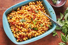 a blue bowl filled with pasta and spinach on top of a wooden table