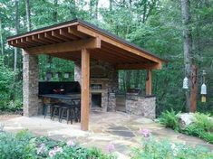 an outdoor kitchen and grill area in the middle of a wooded area with flowers around it