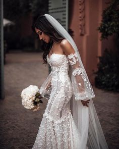 a woman in a wedding dress and veil walking down the street with flowers on her bouquet