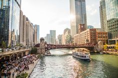 a boat is going down the river in front of some tall buildings and people walking