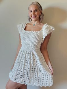 a woman standing in front of a wall wearing a white crochet dress with short sleeves