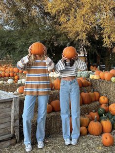 two people standing next to each other in front of pumpkins