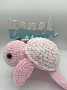 a pink and white crocheted turtle sitting on top of a wooden stand next to a sign