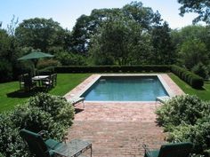 an outdoor swimming pool surrounded by lush green trees and shrubs, with chairs around it