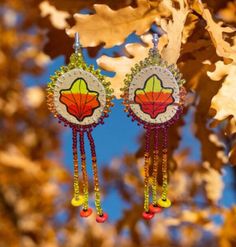 two pairs of earrings hanging from a tree branch with leaves in the sky behind them