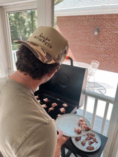 a man wearing a hat is grilling meat on an outdoor grill with a plate