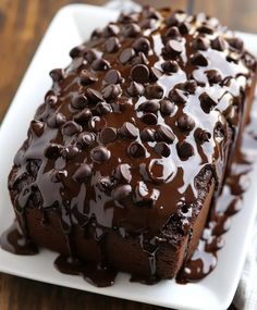 a chocolate cake on a white plate covered in chocolate chips and drizzles