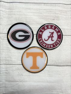 three magnets with the university of georgia, tennessee and letter t on them sitting on top of a white wooden surface