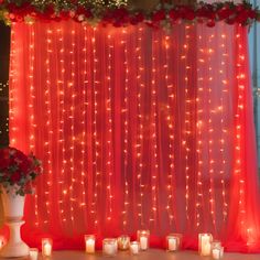 candles are lit in front of a red curtain with roses and greenery on it