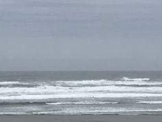 two surfers in wetsuits carrying their surfboards out to the ocean on a cloudy day