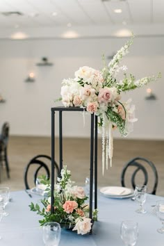 an elegant centerpiece with flowers and greenery sits on a blue table cloth at the reception