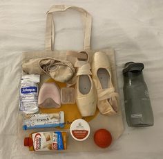 an assortment of items are laid out on a bed with a tote bag and water bottle