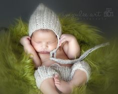 a newborn baby wearing a white knitted hat and diaper is laying on green fur