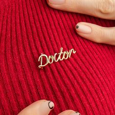 a woman's hand holding a pin with the word doctor written on it in gold