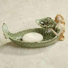 a ceramic mermaid sitting on top of a leaf shaped boat with a candle holder in the shape of a fish