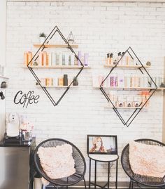 two chairs and a table in front of a white brick wall with shelves on it