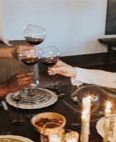 three people are toasting with wine glasses on a dining room table in front of candles