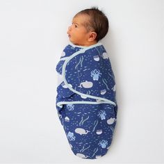 a baby wrapped in a blue blanket laying on top of a white wall next to it's head