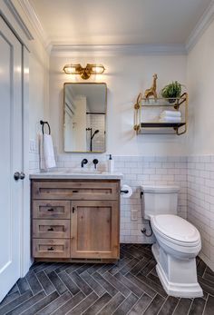 a white toilet sitting next to a wooden sink vanity in a bathroom under a mirror