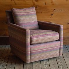 a striped chair sitting on top of a wooden floor next to a wood paneled wall