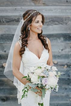 a bride holding her bouquet in front of a rustic wooden wall and wearing a veil