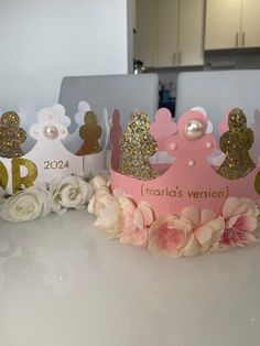 there are three crowns on the table with flowers in front of them and one is pink