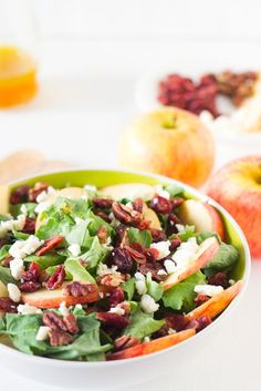 a green bowl filled with salad next to apples