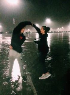 two people are dancing in the rain at night