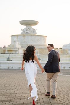 a man and woman holding hands in front of a fountain