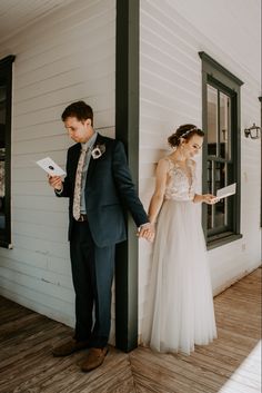 a bride and groom standing on the porch of a house looking at something in their hand