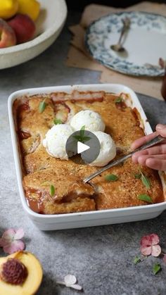 a person cutting into a dish with ice cream and peaches on the table next to it