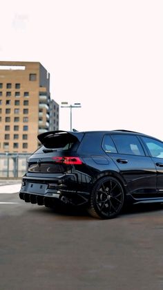 the back end of a black car parked in a parking lot next to tall buildings