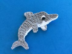 a crocheted dolphin brooch sits on a blue background